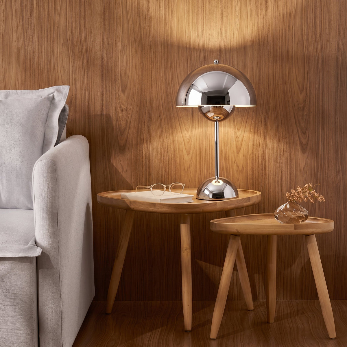 A chrome Oaklume Dome lamp lit on a side table in a wood-panelled living room