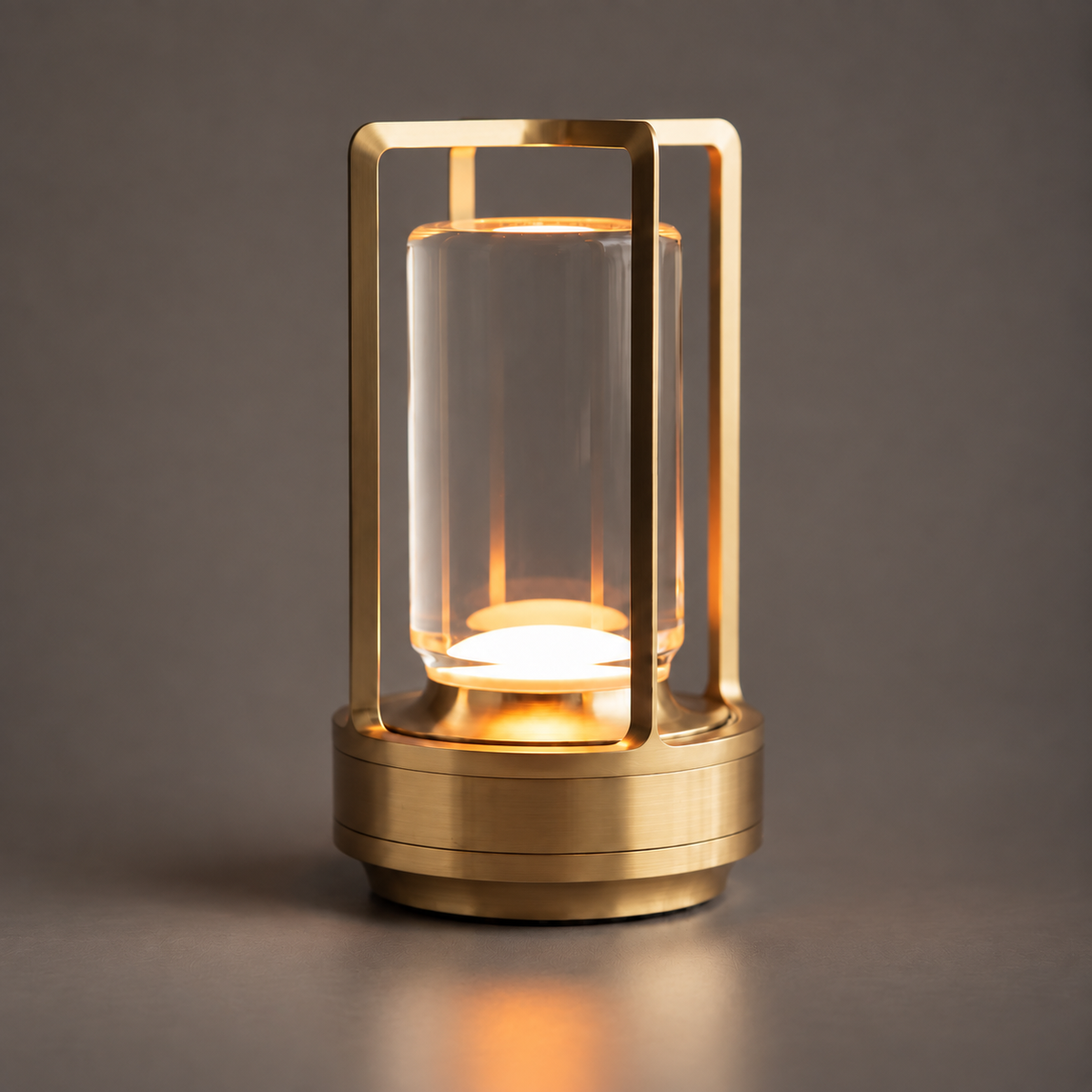 A gold cordless lantern lamp with a clear cylinder, lit from the base